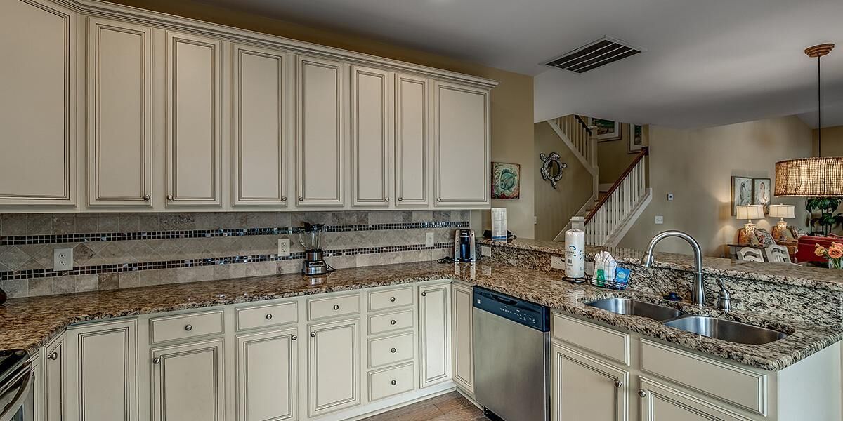 A kitchen with white cabinets, granite countertops, a dishwasher, and a stainless steel sink.