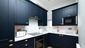 Une cuisine moderne avec des meubles de couleur bleu foncé, un plan de travail blanc, un four encastré, un four à micro-ondes et un grille-pain.