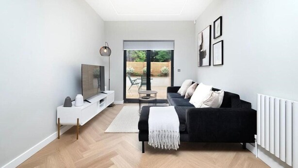 Un salon moderne avec un canapé noir, un meuble TV blanc et une grande fenêtre.