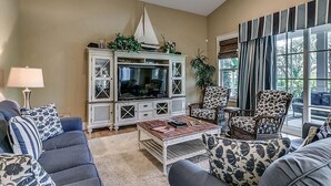Una sala de estar con televisor, dos sillones estampados, un sofá y una mesa de centro.