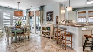 A spacious kitchen with a dining area, featuring a large island with stools, a chandelier, and a view of the outdoors through large windows. - Unrivaled Luxury 3BR Home with Private Pool (North Myrtle Beach)