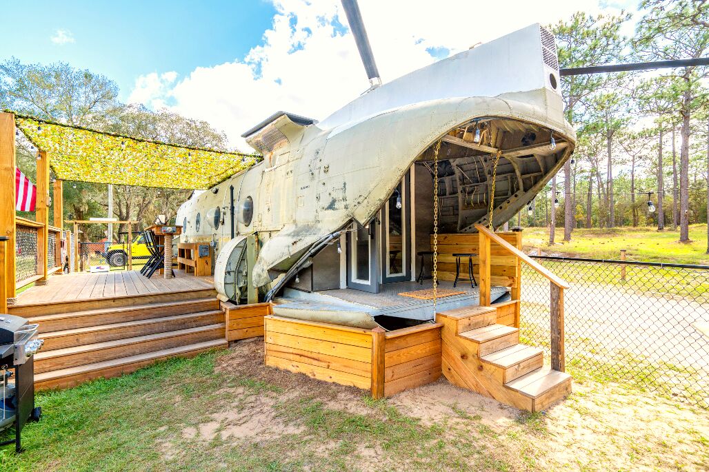 Un grand avion blanc d’époque, doté d’un pont en bois et d’escaliers menant à l’intérieur, entouré d’une clôture et d’arbres.