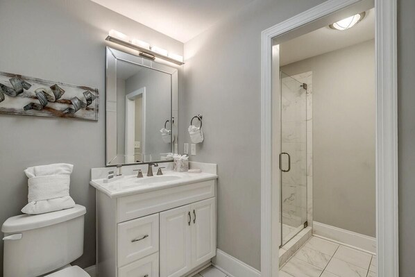 Un baño moderno con un tocador blanco, un espejo grande y una ducha con cerramiento de vidrio.