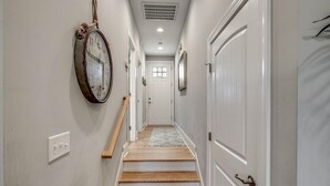 A hallway with a wooden staircase, white walls, and a hanging clock.