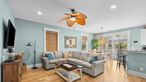 A modern living room with a sectional sofa, a coffee table, a ceiling fan, and a kitchen area with a bar. - Unwind in Style: Luxury 2 Bdrm Townhome Sleeps 8 (North Myrtle Beach)