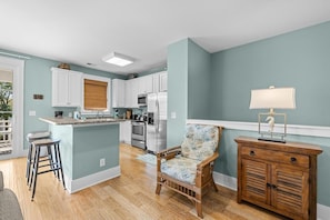 A kitchen with white cabinets, a wooden island, and a chair with a floral pattern. - Unwind in Style: Luxury 2 Bdrm Townhome Sleeps 8 (North Myrtle Beach)