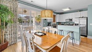A modern kitchen with white cabinets, stainless steel appliances, and a wooden dining table with chairs. - Unwind in Style: Luxury 2 Bdrm Townhome Sleeps 8 (North Myrtle Beach)