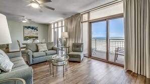 Amplia sala de estar con un ventanal que da a una playa, amoblada con un sofá, sillones y una mesa de centro.