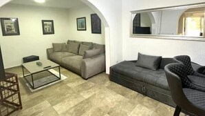 A living room with a sofa, a coffee table, and a TV. There are framed pictures on the wall and a mirror above the sofa. - Apartments Harmonija  (Becici)