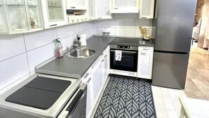 A kitchen with white cabinets, a stainless steel sink, a black refrigerator, and a patterned floor. - Apartments Harmonija  (Becici)