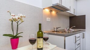 A modern kitchen with a wine bottle and glasses on a tray, a pink potted orchid, and a small table with a candle. - Apartments Harmonija  (Becici)