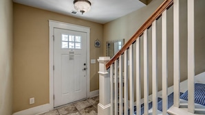 A hallway with a white door, a wooden staircase with white balusters, and a light fixture on the ceiling. - Space, Style, and Serenity: 2 Bdrm Luxury Townhome (North Myrtle Beach)