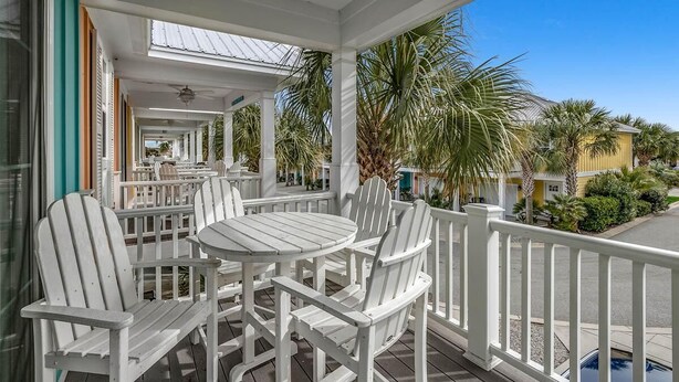 A covered outdoor seating area with white Adirondack chairs and a round table, surrounded by a white railing.