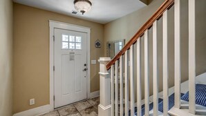 A hallway with a white door, a wooden staircase with white balusters, and a light fixture on the ceiling.
