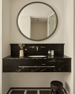 Un baño moderno con un lavabo de mármol negro, un espejo redondo y un taburete pequeño.