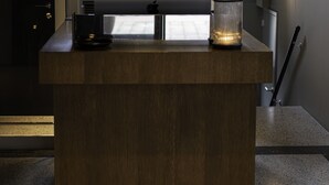 A modern reception desk with a wooden finish, a glass display case, and a decorative light fixture above. - Morgan & Mees Rotterdam (Rotterdam)