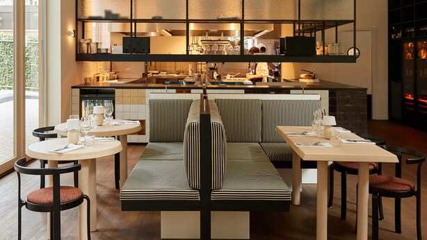 A modern kitchen with a central island, seating area with striped cushions, and a large window overlooking the street. - Morgan & Mees Rotterdam (Rotterdam)