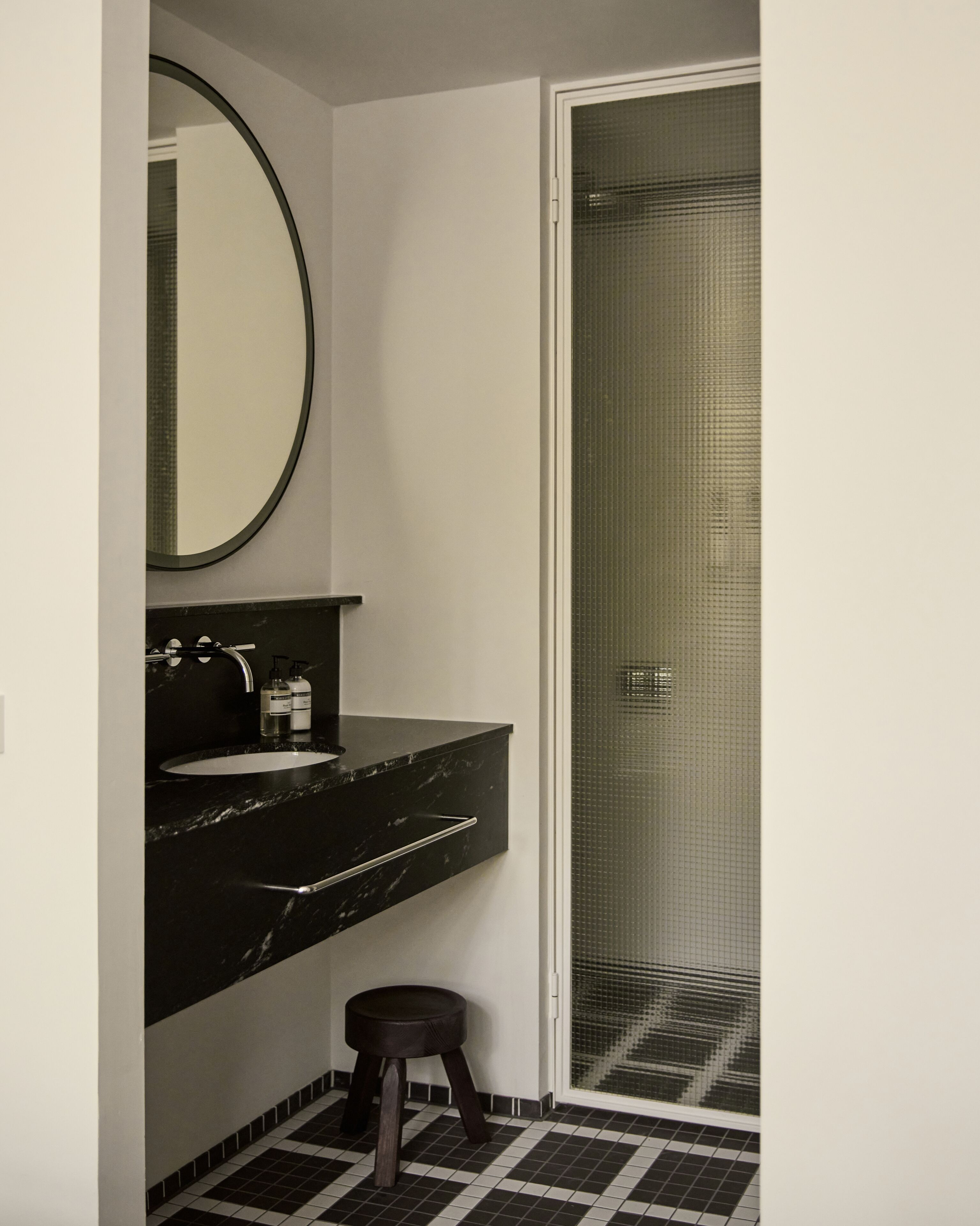 A bathroom with a black marble sink, a round mirror, and a shower with a glass door.