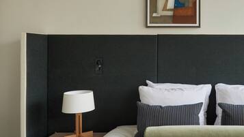 Ein ordentlich bezogenes Bett mit Streifenmuster, eine Nachttischlampe und ein gerahmtes abstraktes Gemälde an der Wand.
