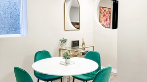 A dining area with a round white table, four green chairs, a potted plant, and a gold-framed mirror on the wall. - Charming 2BR Home | Sleeps 5| Full Stock Kitchen (Drumheller)