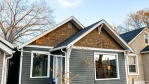 A single-story house with a front porch, a garage, and a small yard. - Charming 2BR Home | Sleeps 5| Full Stock Kitchen (Drumheller)