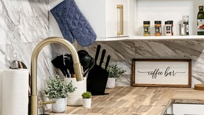 A modern kitchen with marble walls, a wooden countertop, a gold faucet, and a 'coffee bar' sign. - Charming 2BR Home | Sleeps 5| Full Stock Kitchen (Drumheller)