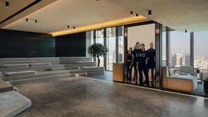 Um hall amplo com design moderno, apresentando uma grande área de estar, uma escadaria e vista para a cidade através de amplas janelas.