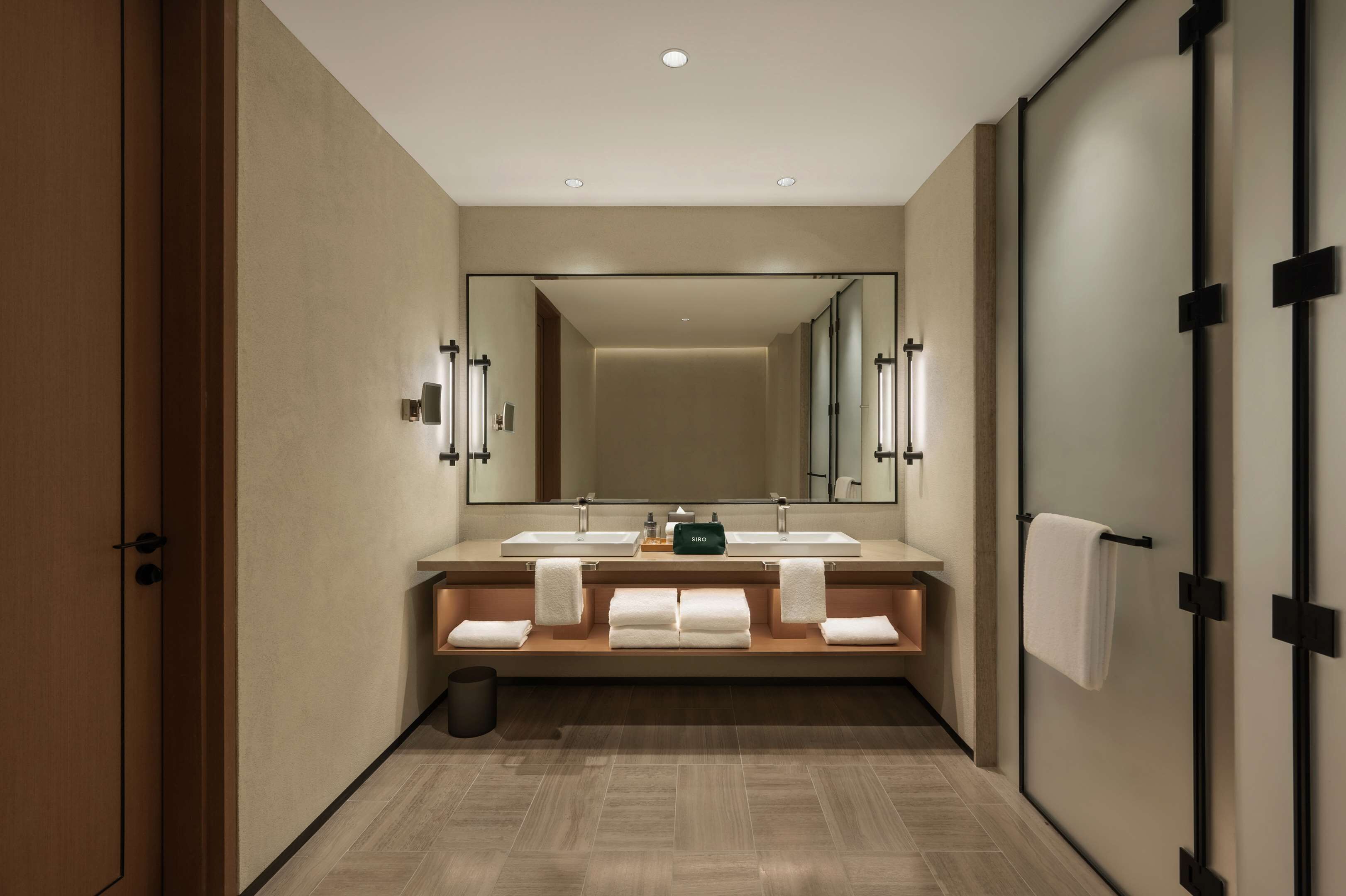 Un baño moderno con un espejo grande, dos lavamanos y un perchero para toallas.