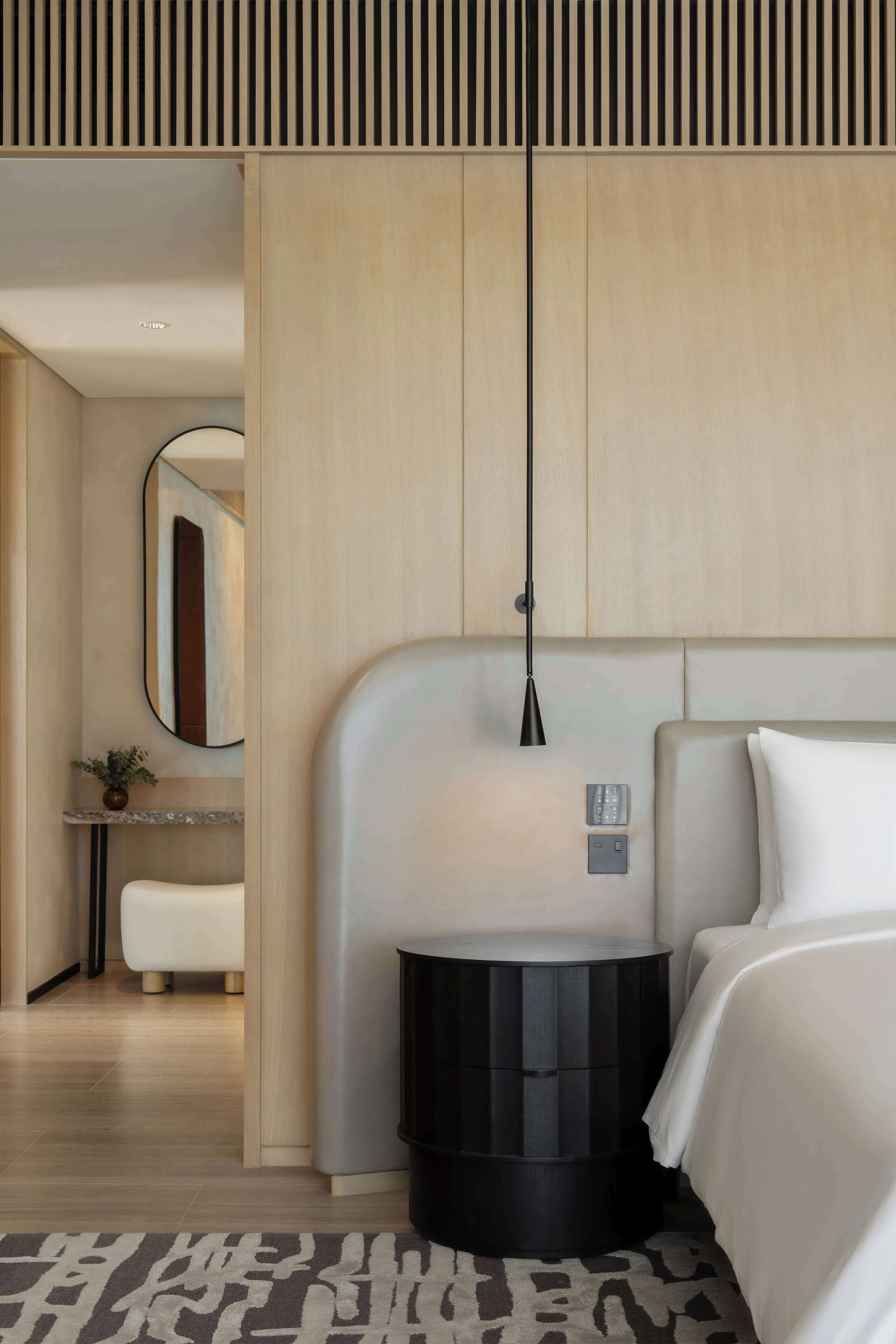 A modern hotel room with a bed, bedside table, and a wall-mounted lamp.