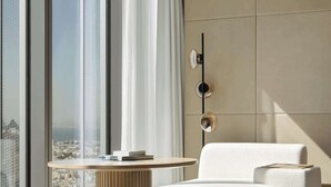 Uma sala de estar moderna com uma grande janela, uma mesa redonda de madeira, um sofá branco e um tapete estampado.