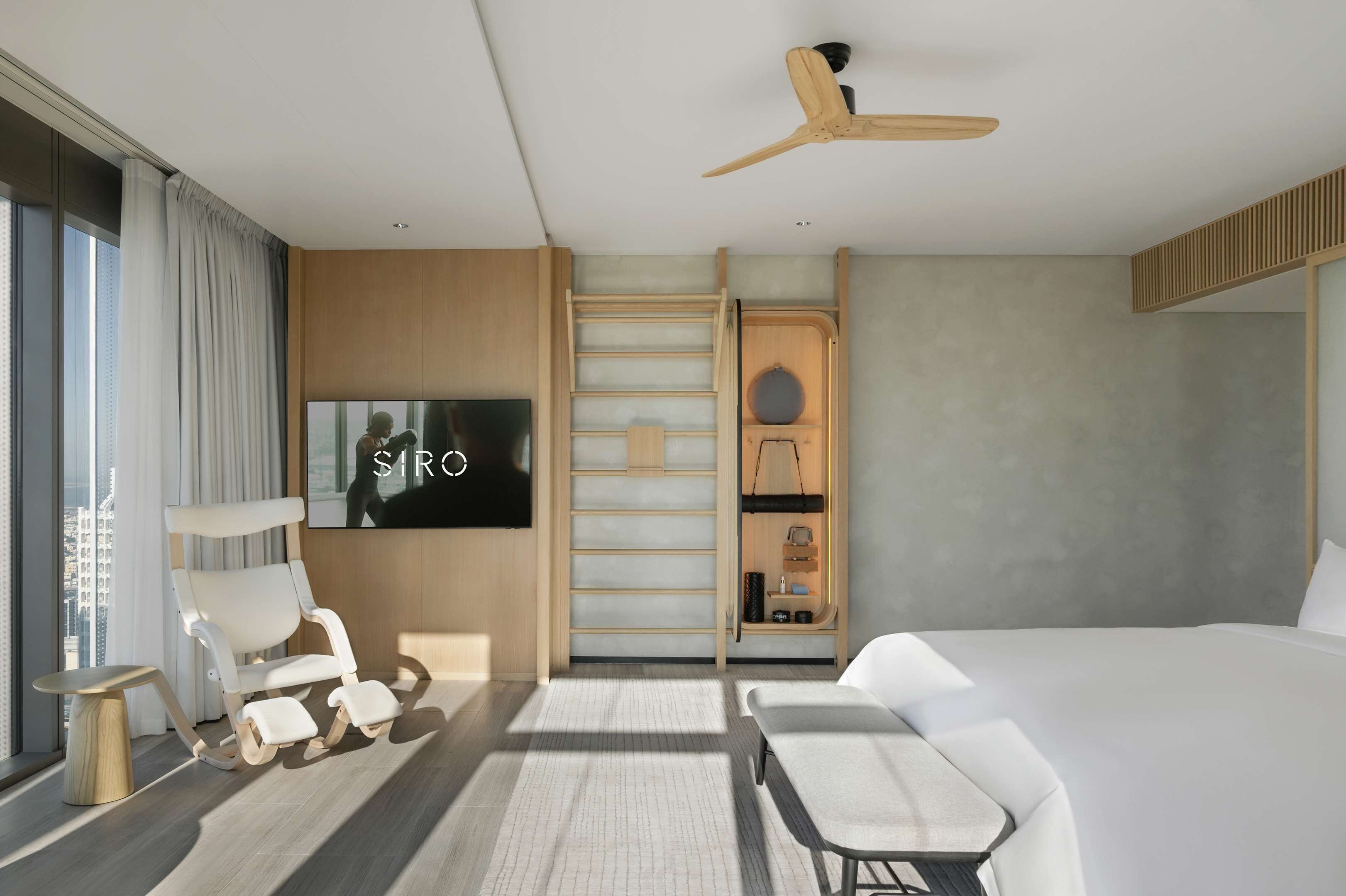 A modern hotel room with a large bed, a TV, a ceiling fan, and a seating area with a table and chairs.