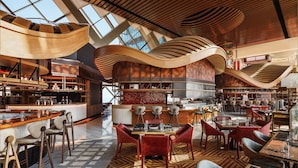 Restaurante moderno com teto alto, ripas de madeira e um espaço de bar central.