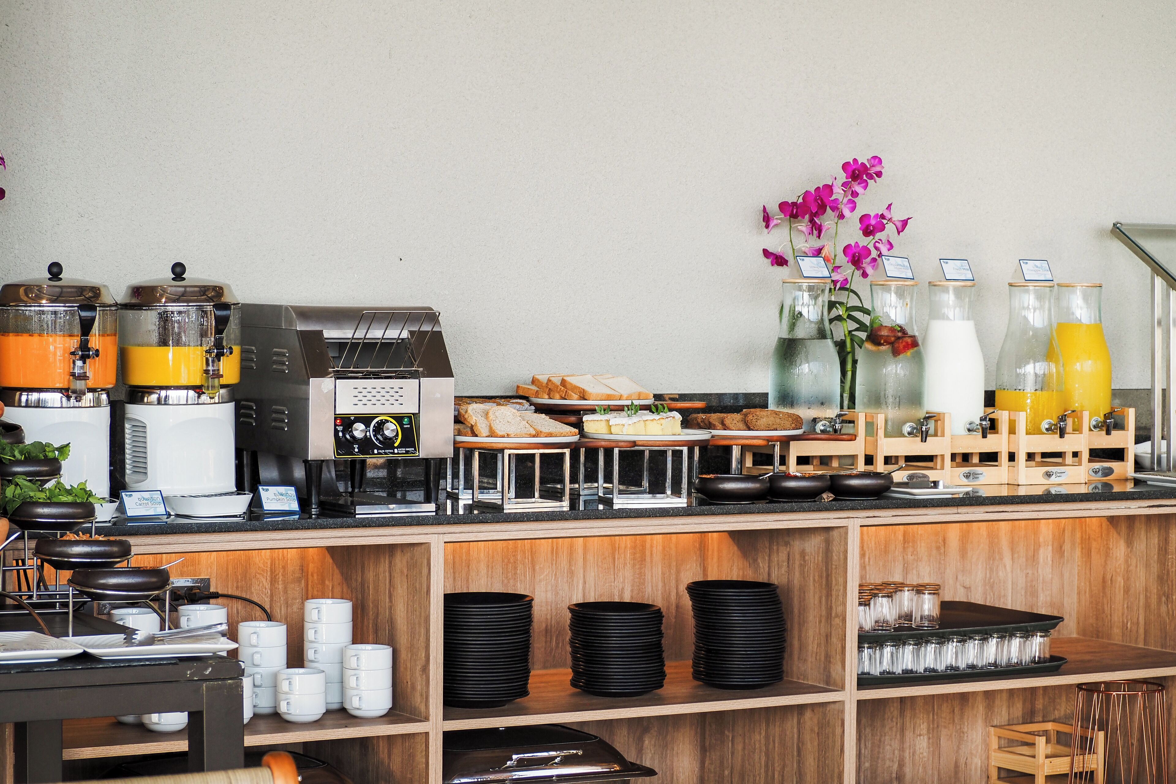 Una barra de desayuno con máquinas de café, una exhibición de frutas y un arreglo floral.