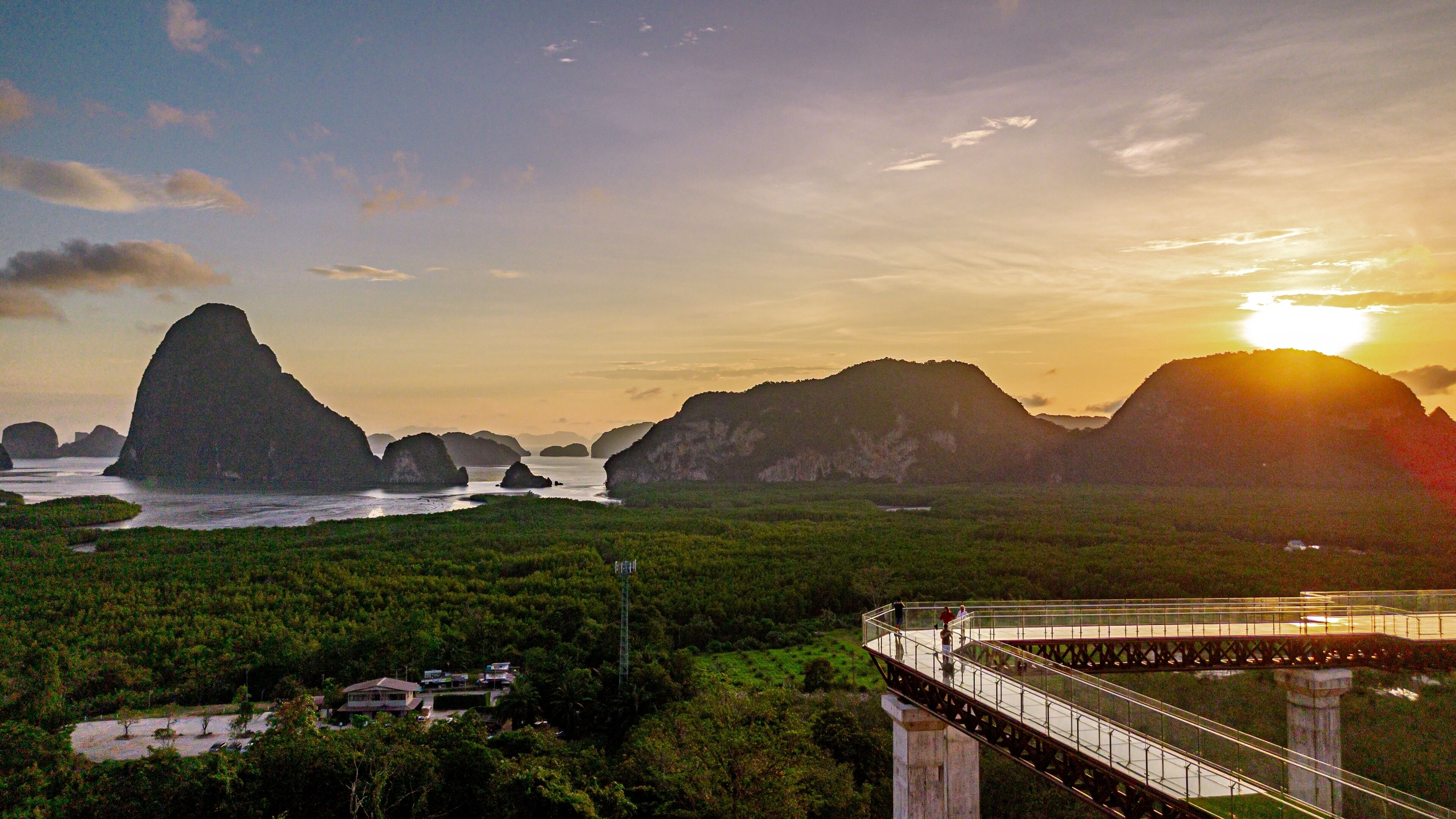 A coastal landscape with a bridge, lush greenery, and distant mountains.