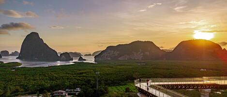 A coastal landscape with a bridge, lush greenery, and distant mountains.