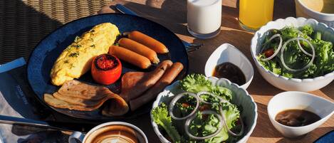 A breakfast setting with a plate of eggs, sausages, and a grilled tomato, accompanied by a glass of milk, a glass of orange juice, a bowl of salad, and a cup of coffee.