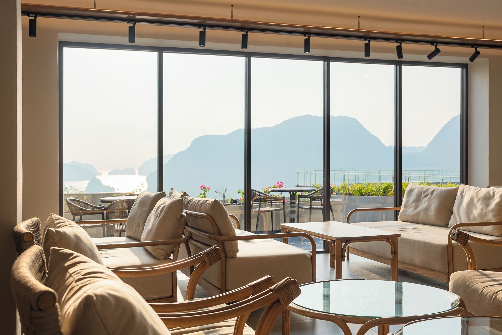 A modern lounge area with a large window offering a mountain view, furnished with sofas and chairs, and a glass table.