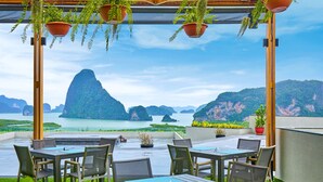 Une terrasse extérieure avec des tables et des chaises, des plantes en pot et une vue sur une baie parsemée d’îles.