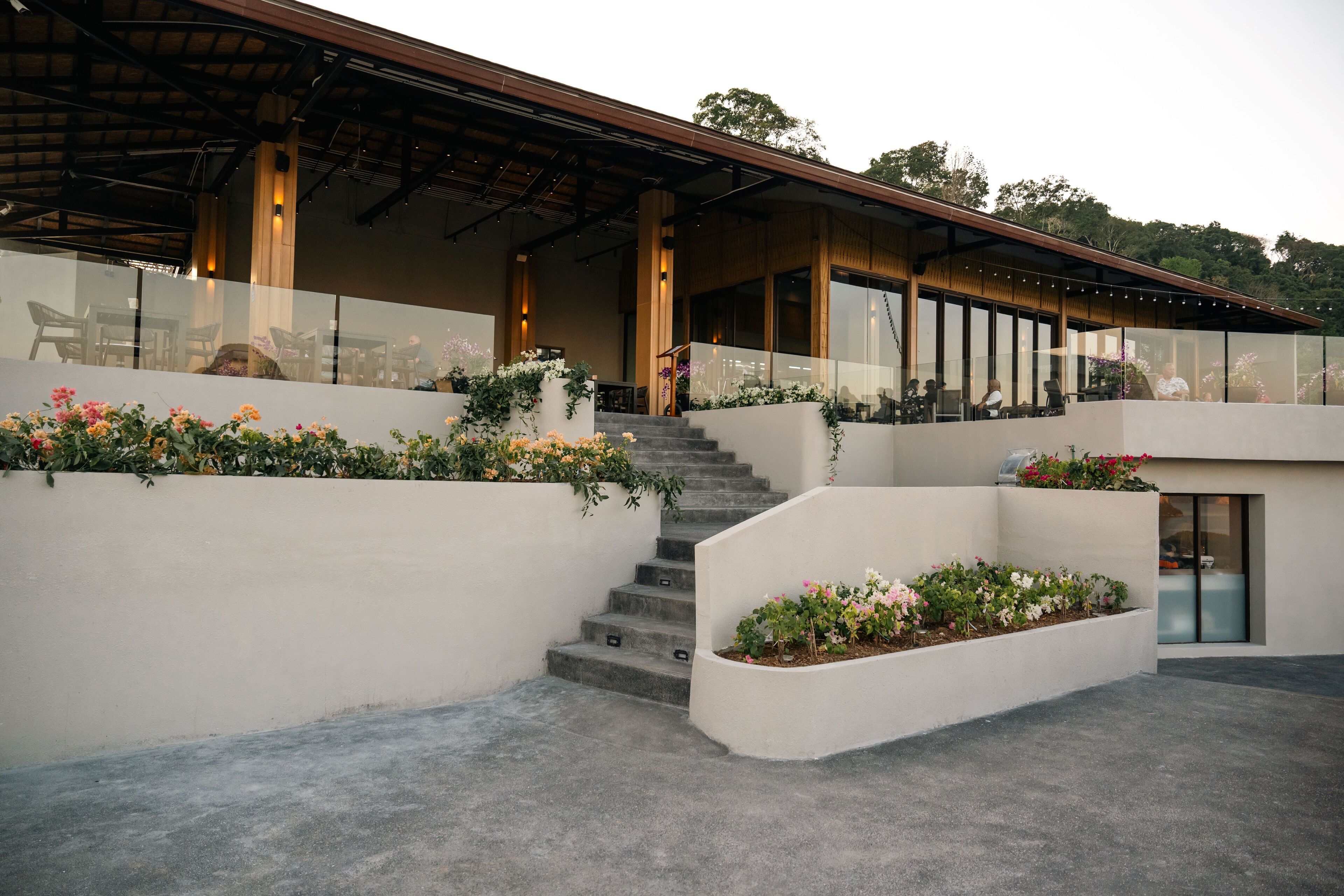 A modern building with a covered outdoor area, a staircase, and flower beds.