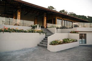 A modern building with a covered outdoor area, a staircase, and flower beds.