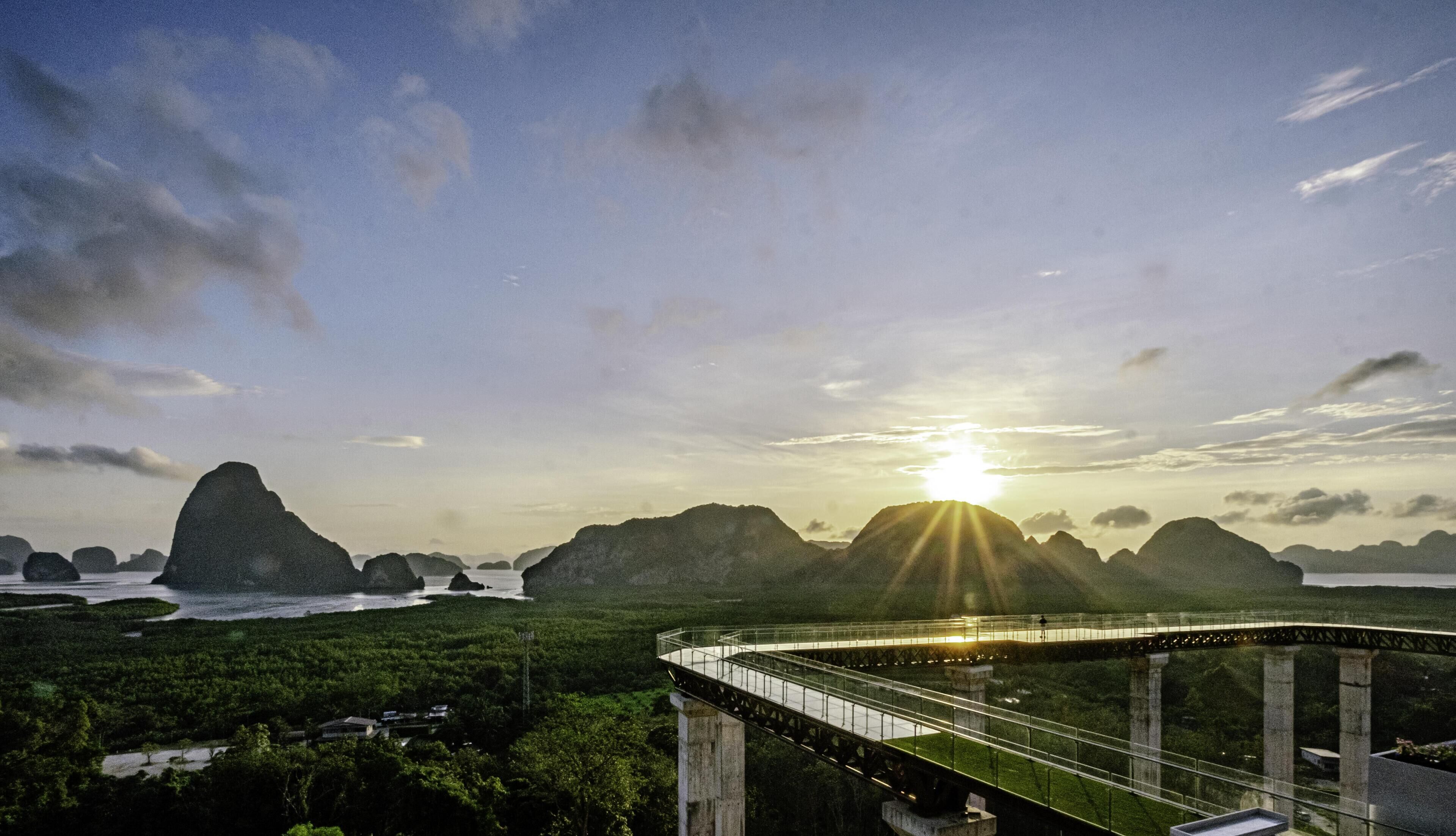 A bridge over a river with a mountainous landscape in the background and the sun setting or rising.