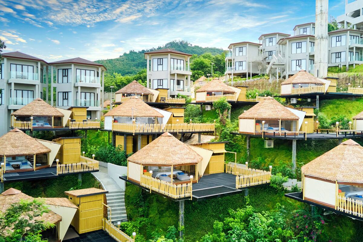 Un resort con varias cabañas, algunas con balcones, ubicado en una ladera con abundante vegetación.