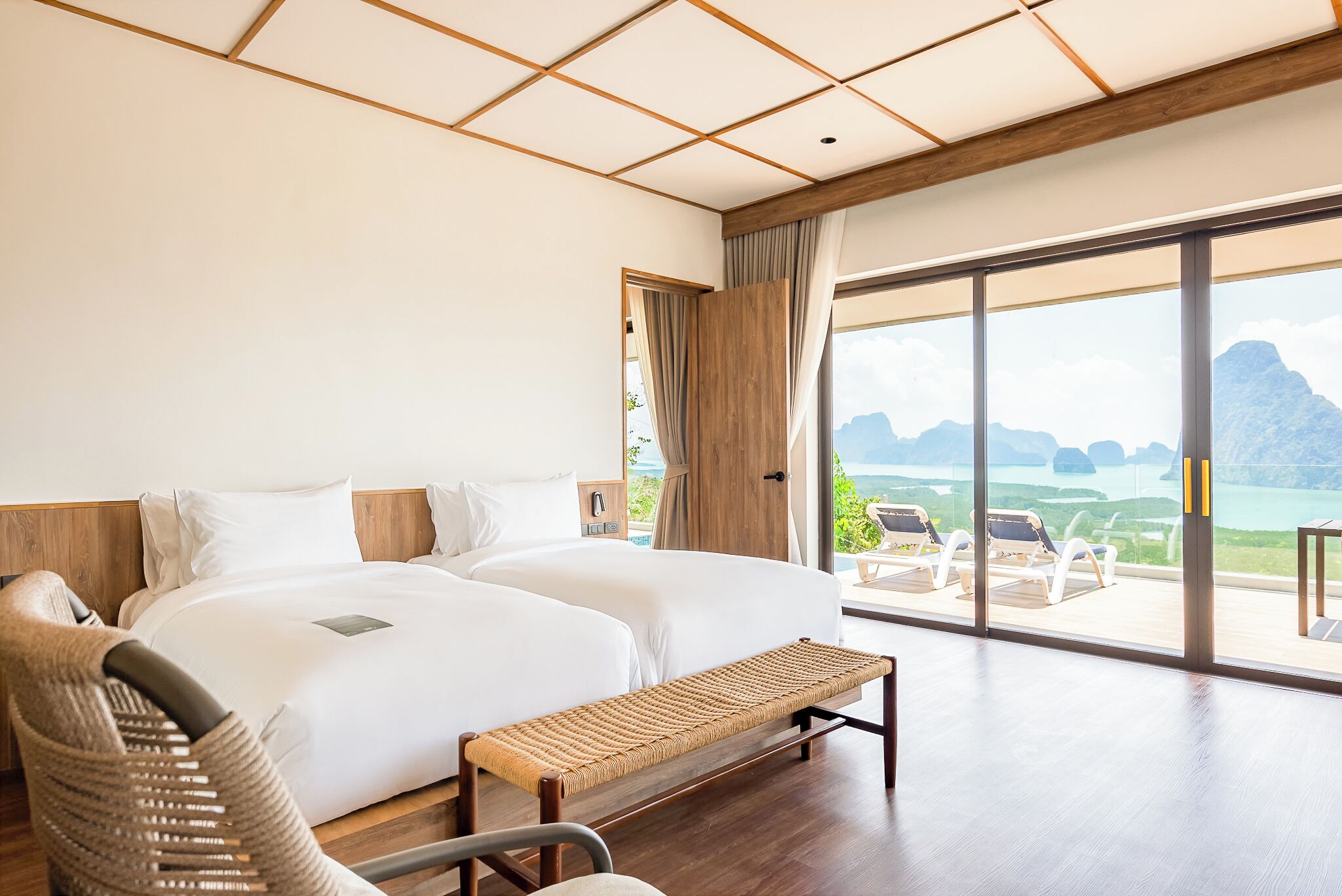 A hotel room with a large bed, a bench, and a view of the mountains and water.