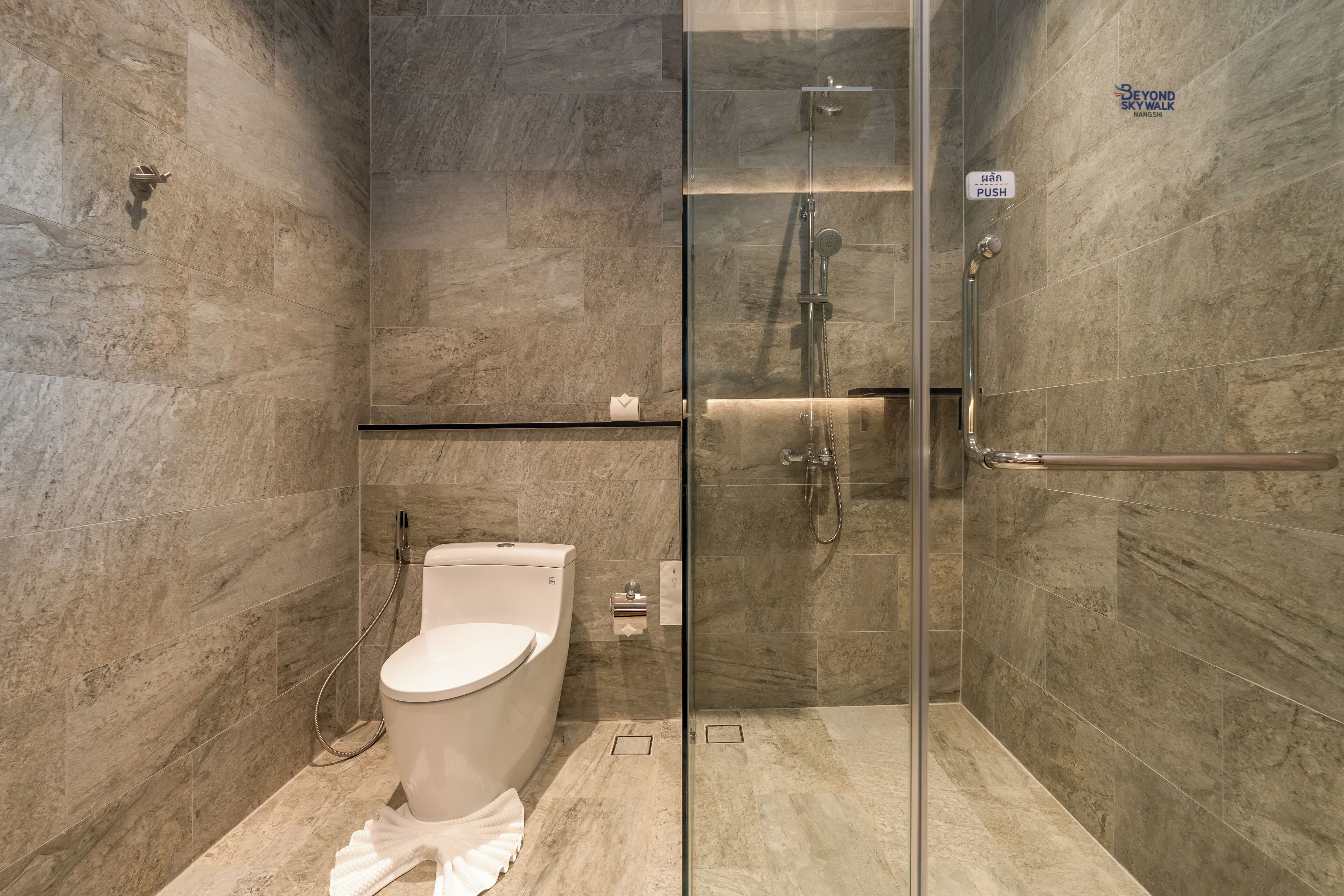 A modern bathroom with a glass shower enclosure, a toilet, and a hand sanitizer dispenser.