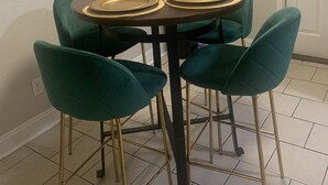 A dining table with four chairs, a broom, and a door in a room with white walls and tiled flooring. - Welcome Home (Charlotte)