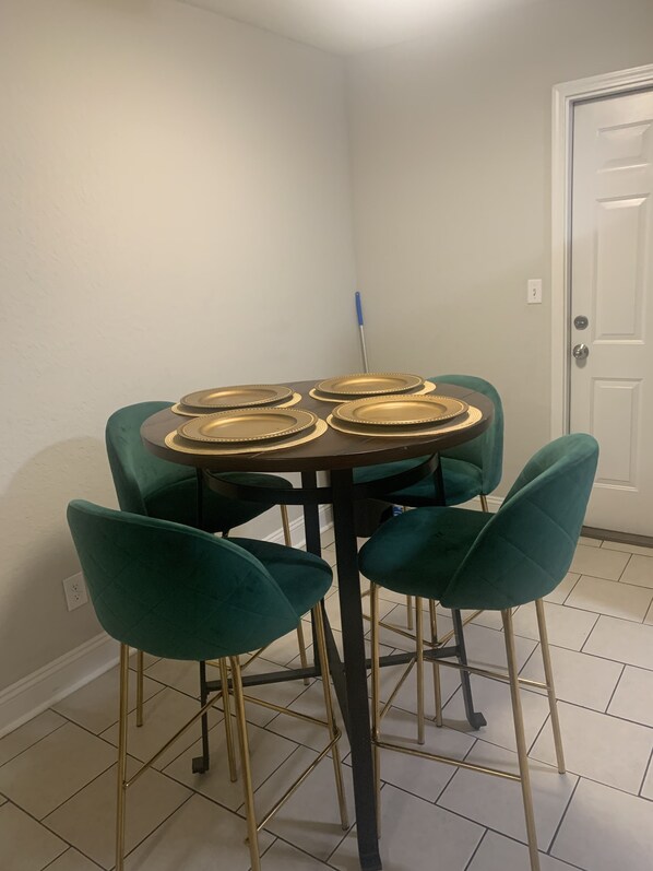 A dining table with four chairs, a broom, and a door in a room with white walls and tiled flooring. - Welcome Home (Charlotte)