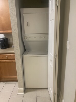 A compact laundry room with a washer and dryer, wooden cabinets, and a tiled floor. - Welcome Home (Charlotte)