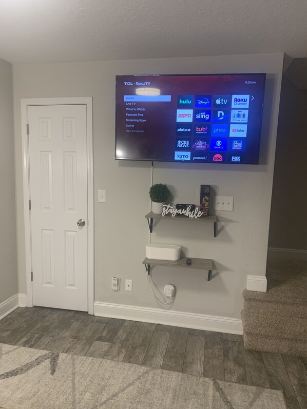 Ein flachbildfernseher an der Wand, der eine Roku TV-Oberfläche mit verschiedenen Streaming-Angeboten zeigt.
