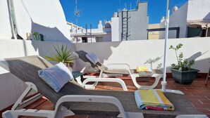 Terraço no telhado com espreguiçadeiras, uma mesa pequena e plantas em vasos.