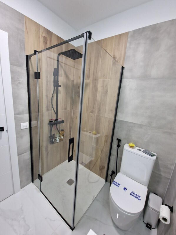 Un baño moderno con ducha acristalada, inodoro y suelo de mármol.